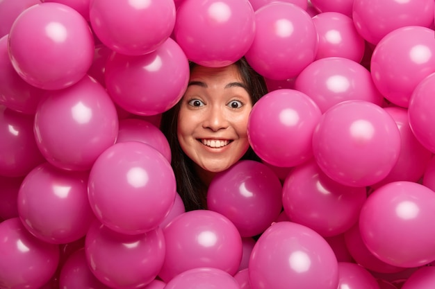 Mulher sorri gentilmente em poses de bom humor em meio a uma pilha de balões cor de rosa inflados