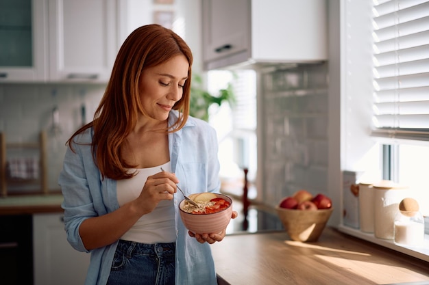 Mulher sorridente a tomar um pequeno-almoço saudável na cozinha