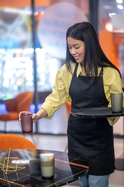 Mulher sorridente abaixando o copo de cappuccino na mesa