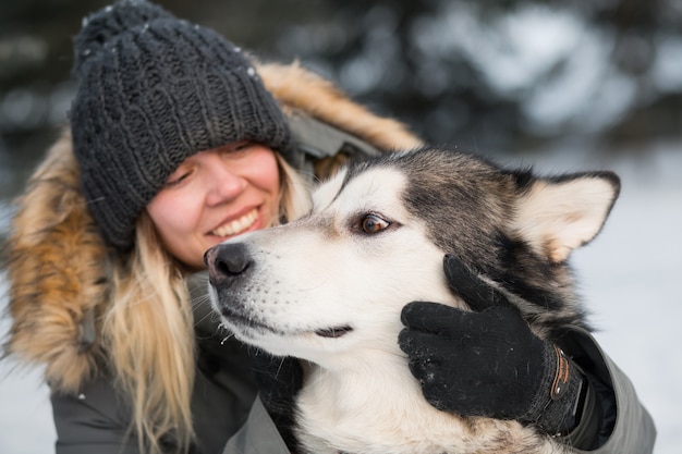 Mulher sorridente abraçando malamute do alasca com amor na floresta de inverno