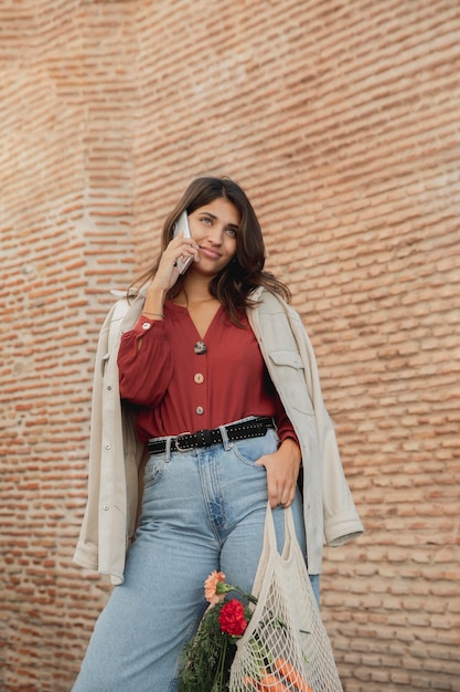 Mulher sorridente ao ar livre com sacolas de compras e smartphone