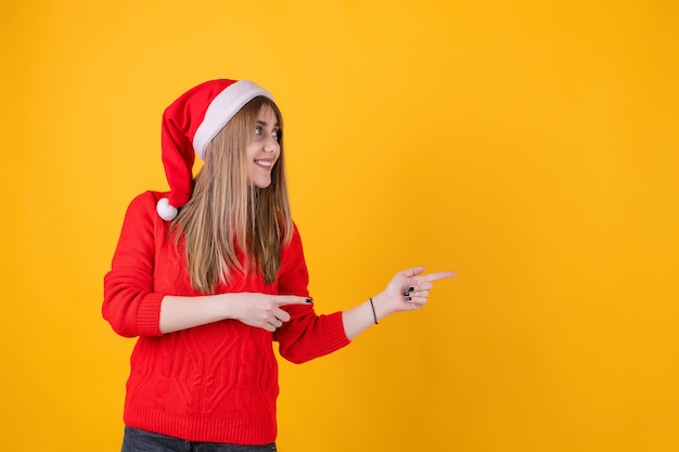 Mulher sorridente, apontando os dedos no espaço da cópia, vestindo chapéu de Papai Noel e camisola vermelha