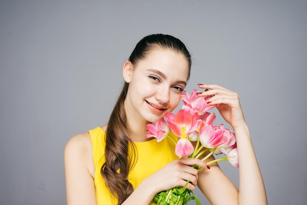 Mulher sorridente atraente em vestido amarelo segurando flores rosa perfumadas e poses