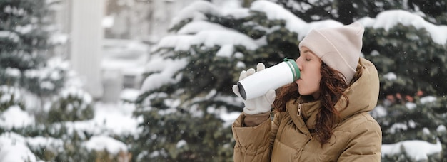 Mulher sorridente bebendo bebida quente de garrafa térmica ao ar livre no inverno