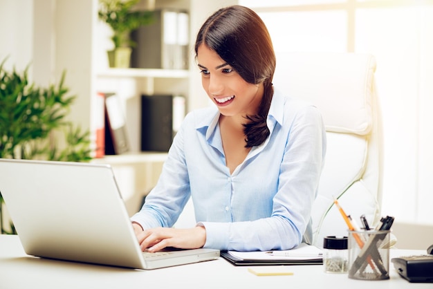 Mulher sorridente bem sucedida usando laptop no escritório.