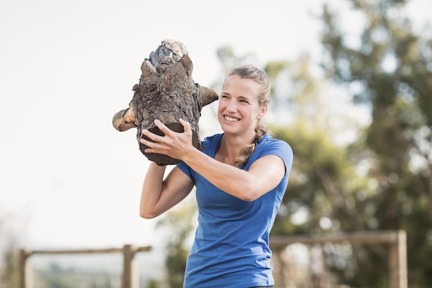 Foto mulher sorridente carregando pesadas toras de madeira durante a pista de obstáculos no campo de treinamento