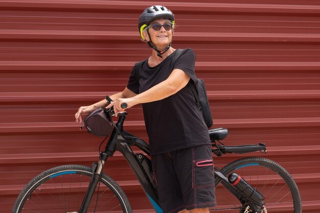 Mulher sorridente ciclista sênior em excursão ao ar livre na cidade urbana com sua bicicleta elétrica Estilo de vida saudável para aposentados e conceito de mobilidade sustentável