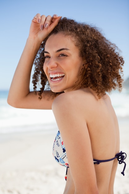 Mulher sorridente colocando sua mão em sua testa enquanto está de pé na praia