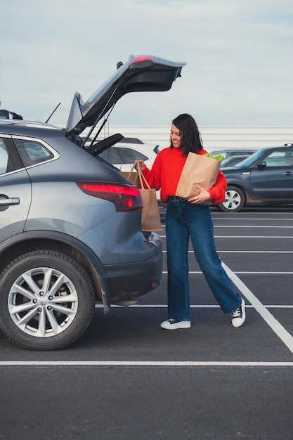 Mulher sorridente colocou sacos no porta-malas do carro para fazer compras.