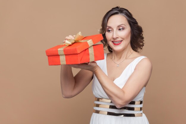 Mulher sorridente com cabelo ondulado abre caixa de presente olhando para dentro sendo interessante o que está dentro