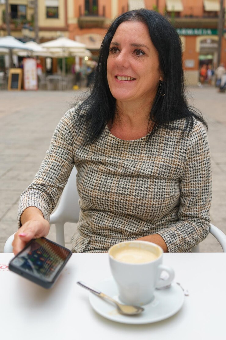 Foto mulher sorridente com cabelo preto segurando um smartphone em um café ao ar livre na cidade