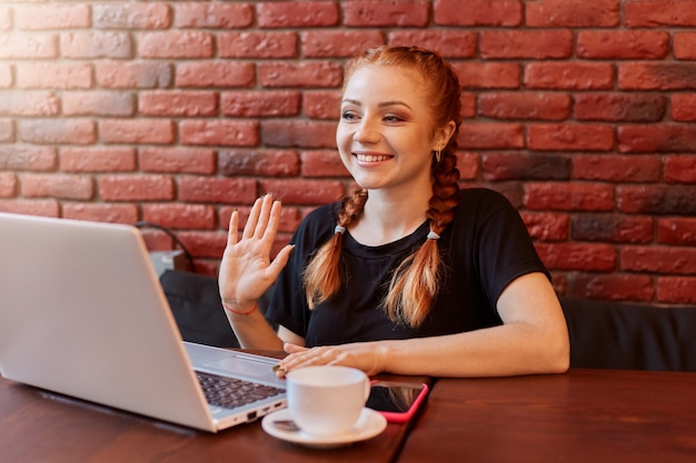 Mulher sorridente com cabelo ruivo e rabo de cavalo engraçado fazendo videochamada no laptop