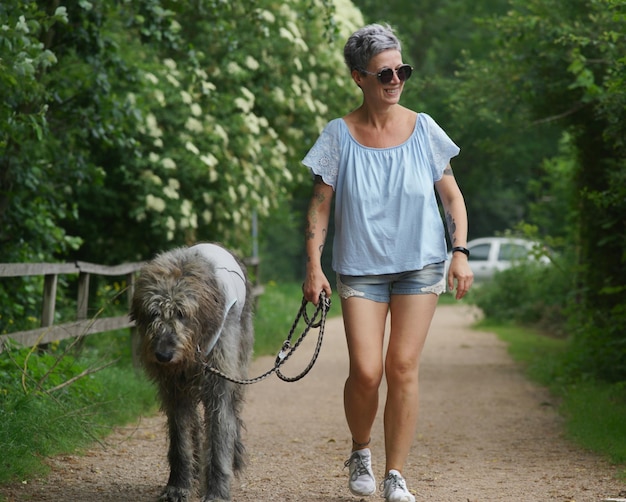 Foto mulher sorridente com cão a caminhar por uma estrada de terra.