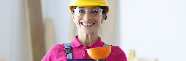 Mulher sorridente com capacete amarelo e óculos, segurando o êmbolo na mão. Serviços de mulher conceito de encanamento