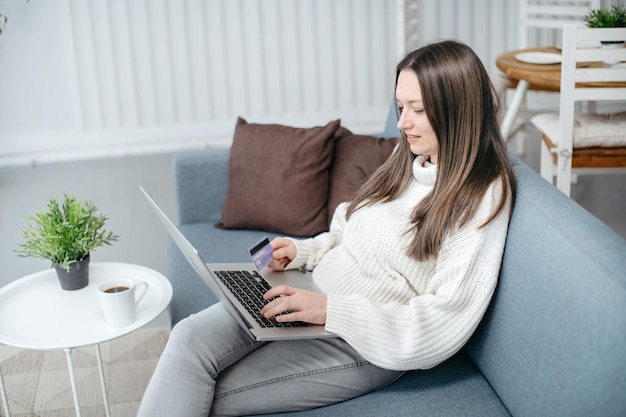 Mulher sorridente com cartão de crédito usando um laptop em uma aconchegante sala de estar