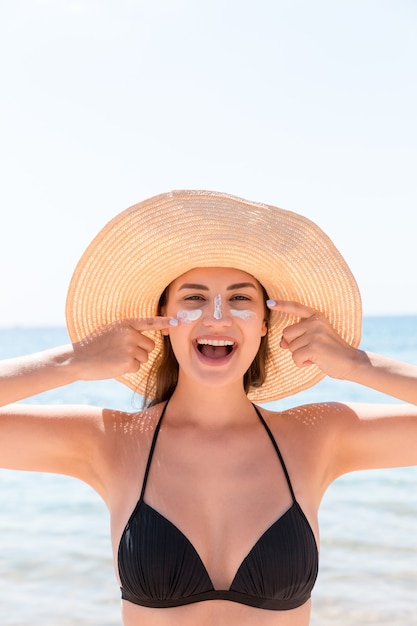 Mulher sorridente com chapéu está aplicando protetor solar no rosto. estilo indiano.