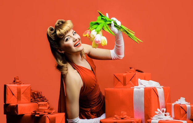 Mulher sorridente com flores da primavera linda loira de vestido vermelho com presente e buquê de tulipas