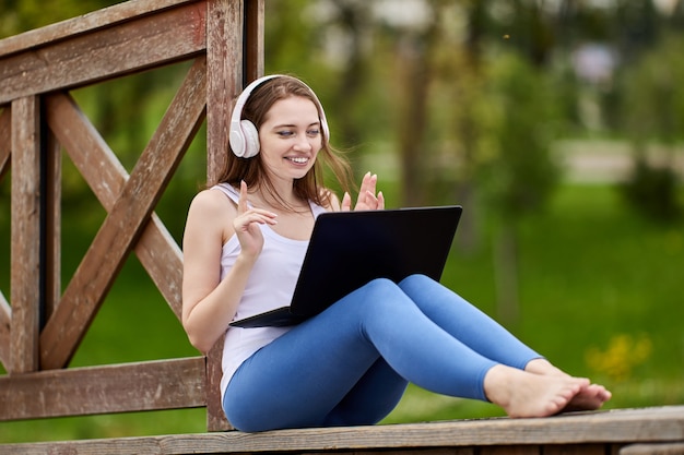 Mulher sorridente com fones de ouvido sem fio trabalha com laptop on-line no parque