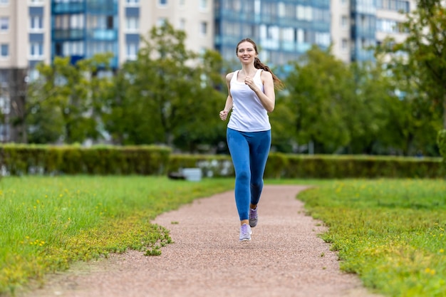 Mulher sorridente com leggins correndo no jardim da cidade pela manhã