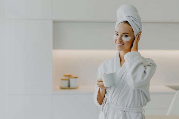 mulher sorridente com manchas de hidrogel sob os olhos aprecia um chá quente