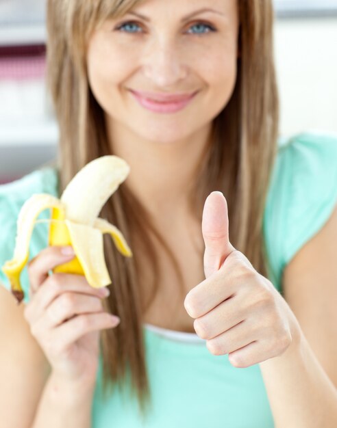 Foto mulher sorridente com o polegar para cima segurando uma banana na cozinha