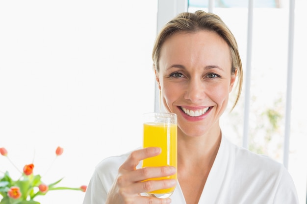 Mulher sorridente com roupão de banho com copo de suco de laranja