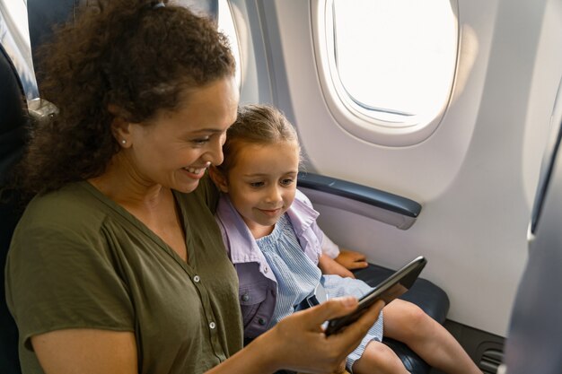 Mulher sorridente com seu filho sentado no avião e usando o smartphone