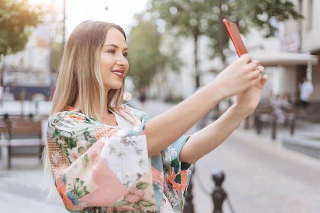 Mulher sorridente com um smartphone tirando uma selfie em uma rua da cidade