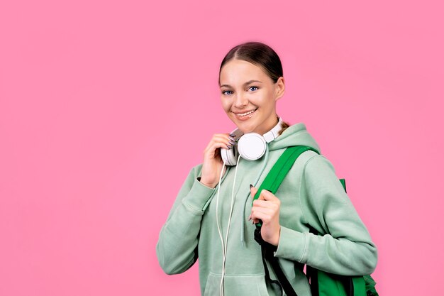 Mulher sorridente com uma mochila e fones de ouvido em uma parede rosa.