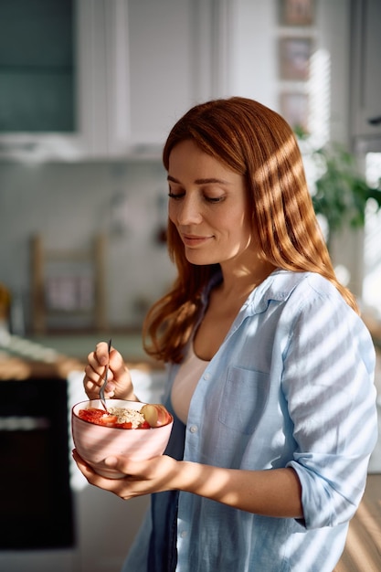 Mulher sorridente comendo aveia com frutas frescas pela manhã