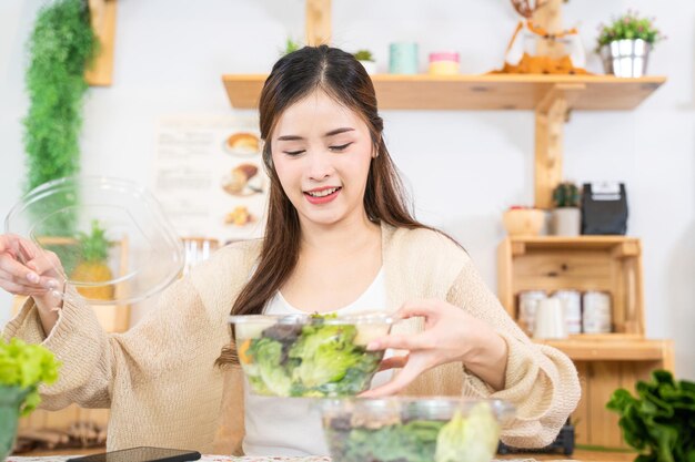 Mulher sorridente comendo legumes frescos e saudáveis mulher sentada na despensa em uma bela cozinha interior A comida de dieta limpa de produtos e ingredientes locais Mercado fresco