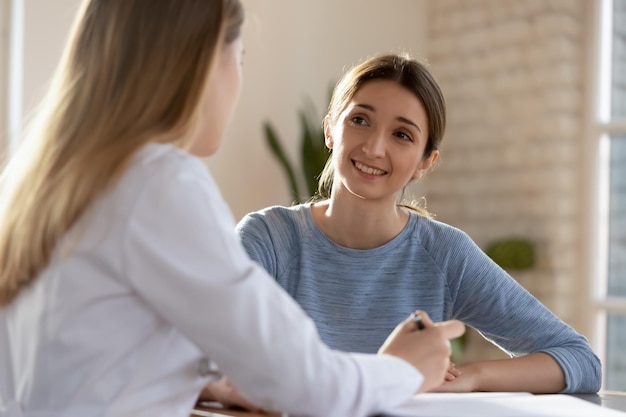 Mulher sorridente da geração do milênio visita uma médica que consulta sobre queixas de saúde feliz cliente jovem satisfeito conversa discute a receita de tratamento com o GP ou médico na consulta no hospital