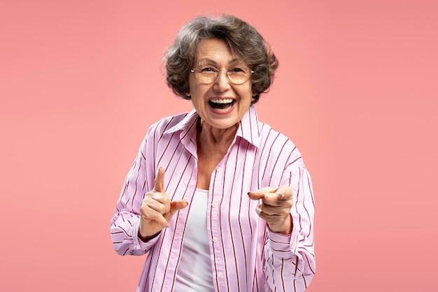 Foto mulher sorridente de 70 anos de idade usando óculos e roupas casuais elegantes apontando dedos