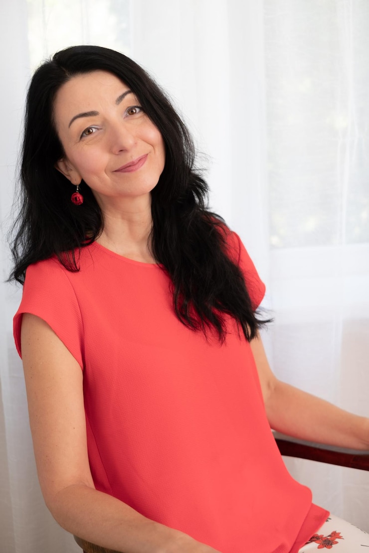 Foto mulher sorridente de camisa vermelha sentada em postura equilibrada expressão confiante ambiente sereno iluminação natural conceito de retrato
