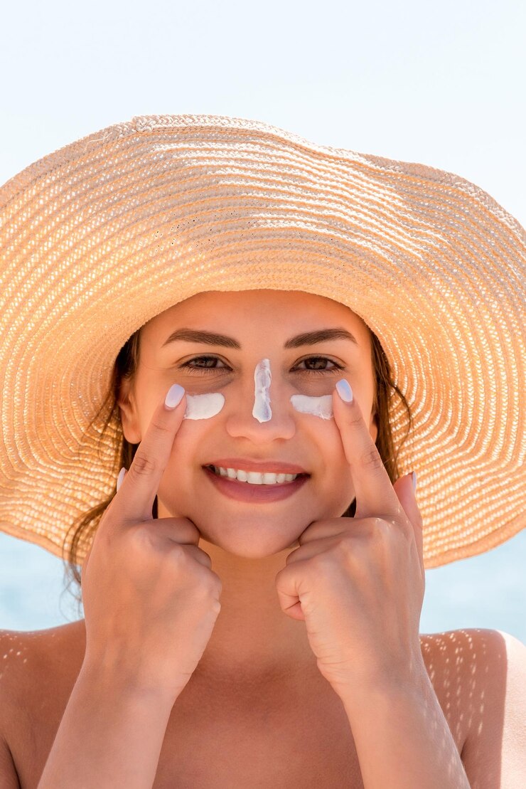 Foto mulher sorridente de chapéu está aplicando protetor solar no rosto estilo indiano