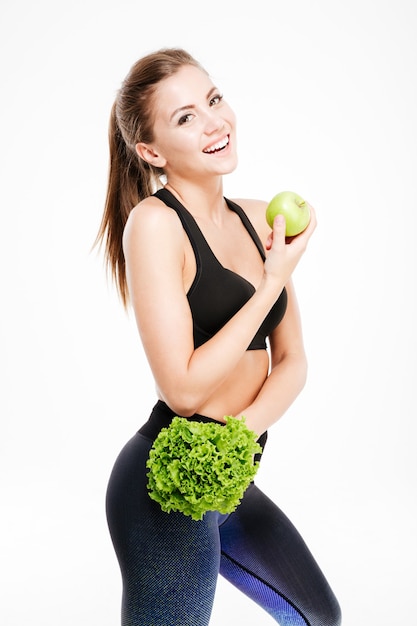 Mulher sorridente de fitness segurando maçã e alface e isolado