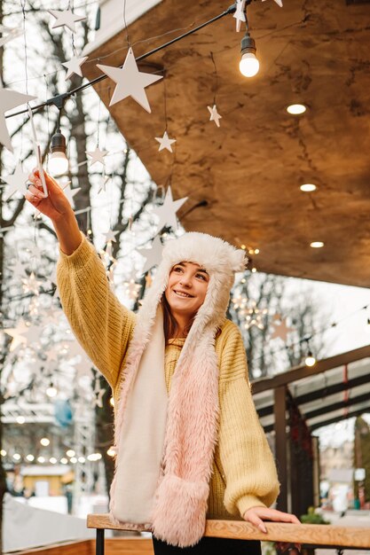 Mulher sorridente de foto vertical comemorando suéter quente vestido e chapéu de lã, posando do lado de fora