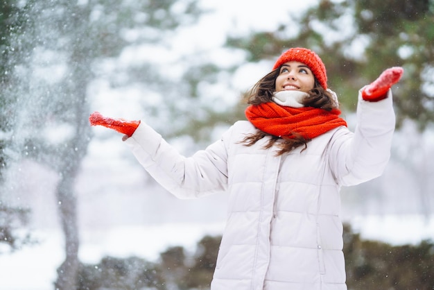 Mulher sorridente de inverno com chapéu vermelho posando em um parque nevado Tempo frio Férias de moda de inverno