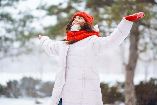 Mulher sorridente de inverno com chapéu vermelho posando em um parque nevado Tempo frio Férias de moda de inverno