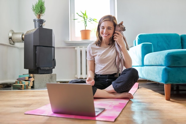 Mulher sorridente de meia idade com laptop e gato no chão