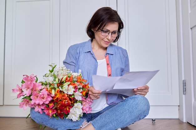 Mulher sorridente de meia-idade com um buquê de flores lendo papel