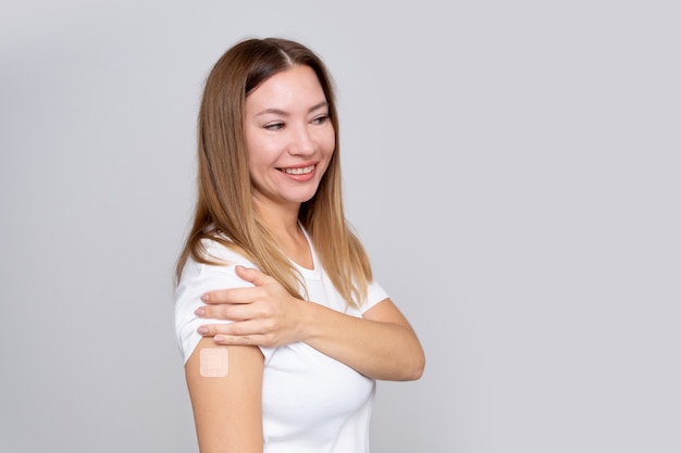 Mulher sorridente de meia-idade com um curativo ou adesivo na mão recebendo uma vacina