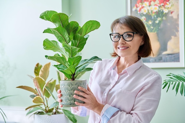 Mulher sorridente de meia-idade com vaso de plantas em casa