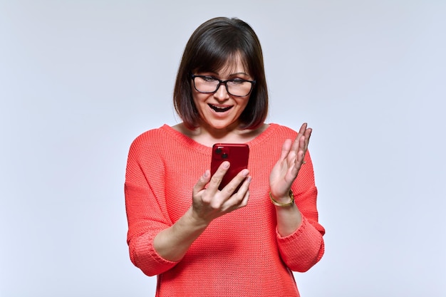 Mulher sorridente de meia idade olhando para o smartphone no fundo do estúdio de luz Linda mulher emocional usando aplicativos on-line móveis Tecnologia estilo de vida internet 40 anos de idade conceito de pessoas