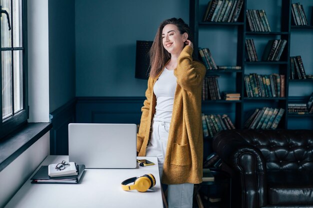 Foto mulher sorridente de pé com tecnologias na mesa em casa