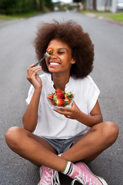 Foto mulher sorridente de tiro completo comendo morangos