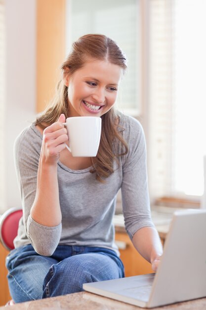 Mulher sorridente desfrutando de café ao digitar em seu laptop