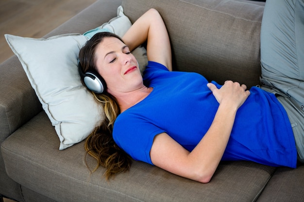 mulher sorridente dormindo no sofá com fones de ouvido