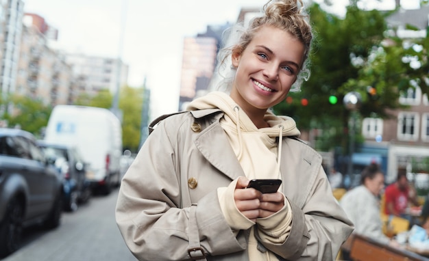 Mulher sorridente e feliz em pé na rua com o telefone celular.