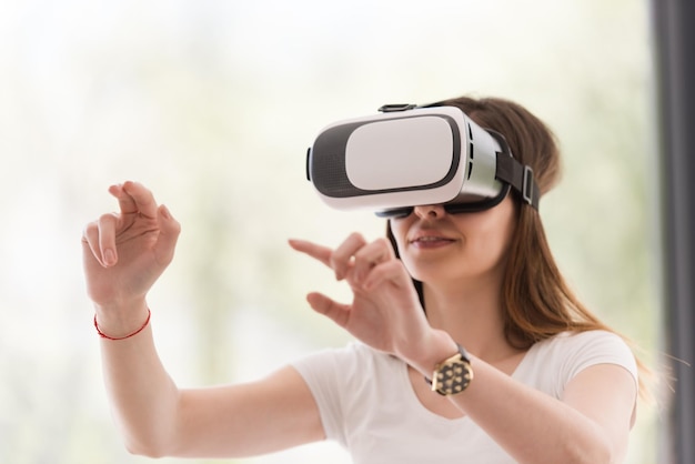 Mulher sorridente e feliz obtendo experiência usando óculos de realidade virtual com fone de ouvido VR em casa